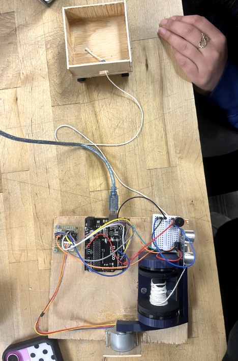 Workbench photo: the wooden sled on wheels above, and below it an Arduino board wired to an ultrasonic sensor, a seven-segment display and a stepper-driven spool.